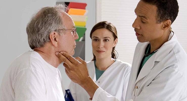 Médico examina el cuello de un adulto mayor mientras otro profesional de salud observa la evaluación clínica.