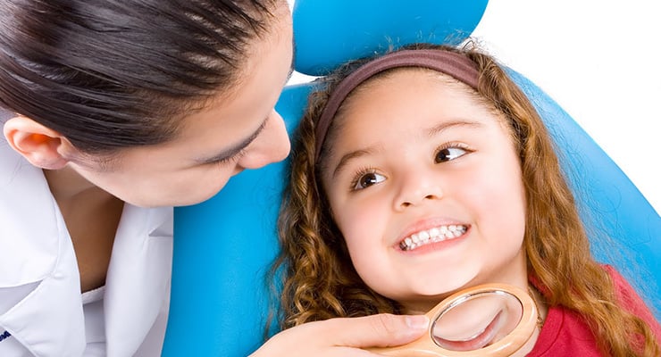 Odontóloga revisa la salud bucal de una niña durante una consulta dental infantil.