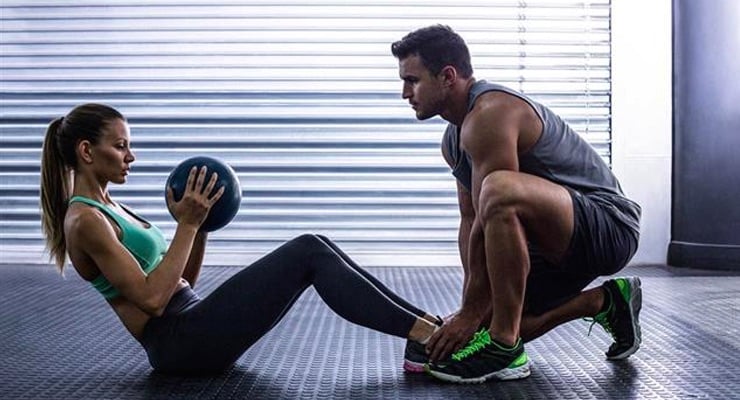 Hombre y mujer realizando ejercicio abdominal con balón medicinal en gimnasio