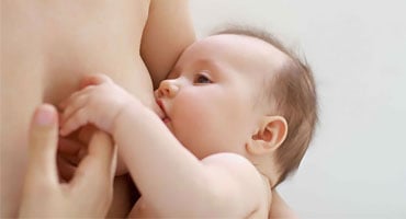 Madre amamantando a su bebé mientras lo sostiene con ambas manos en un entorno tranquilo