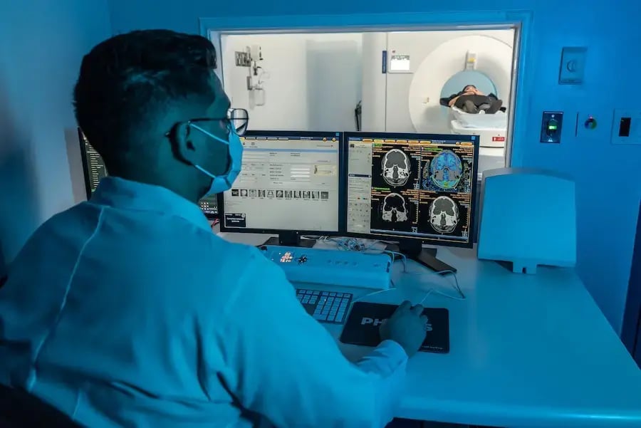 Técnico monitoreando imágenes médicas mientras una paciente realiza un examen en un tomógrafo.