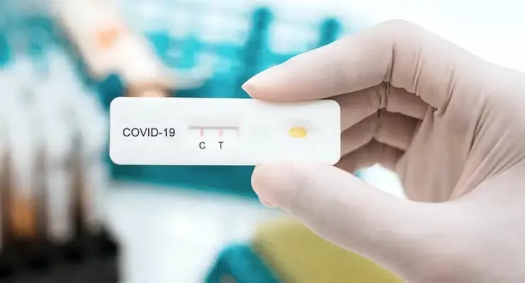 Mano con guante sosteniendo un test rápido de antígeno para COVID-19 con las letras C y T visibles.