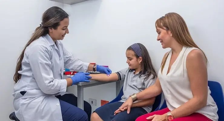 Doctora tomando muestra de sangre a una niña en compañía de su madre en consultorio