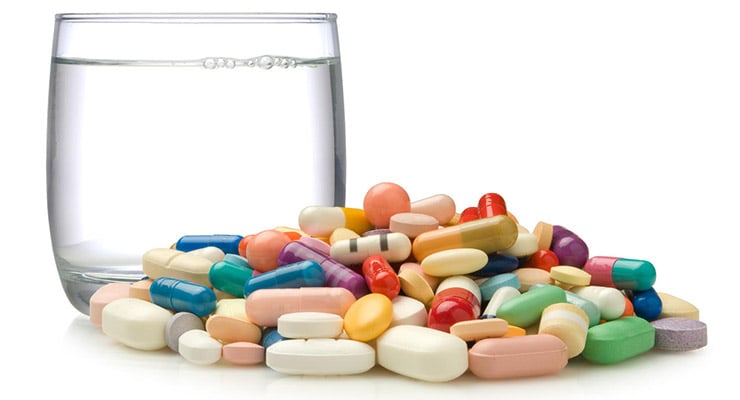 Vasos de agua junto a diferentes pastillas y cápsulas de medicamentos.