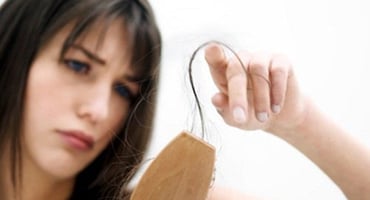 Mujer joven observando con preocupación la pérdida de cabello en su cepillo de madera tras peinarse.