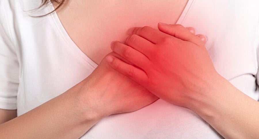 Primer plano de una mujer presionando su pecho con ambas manos, con una zona roja iluminada que simboliza dolor agudo o un síntoma de ataque cardiaco.