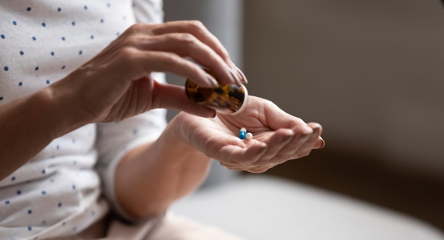 Persona sostiene cápsulas de antibióticos en la mano mientras vierte el medicamento desde un frasco.
