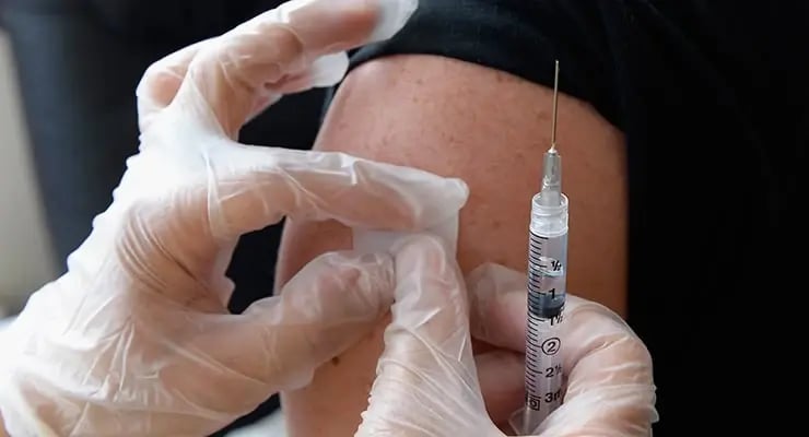Aplicación de vacuna con jeringa en el brazo de una persona por personal de salud