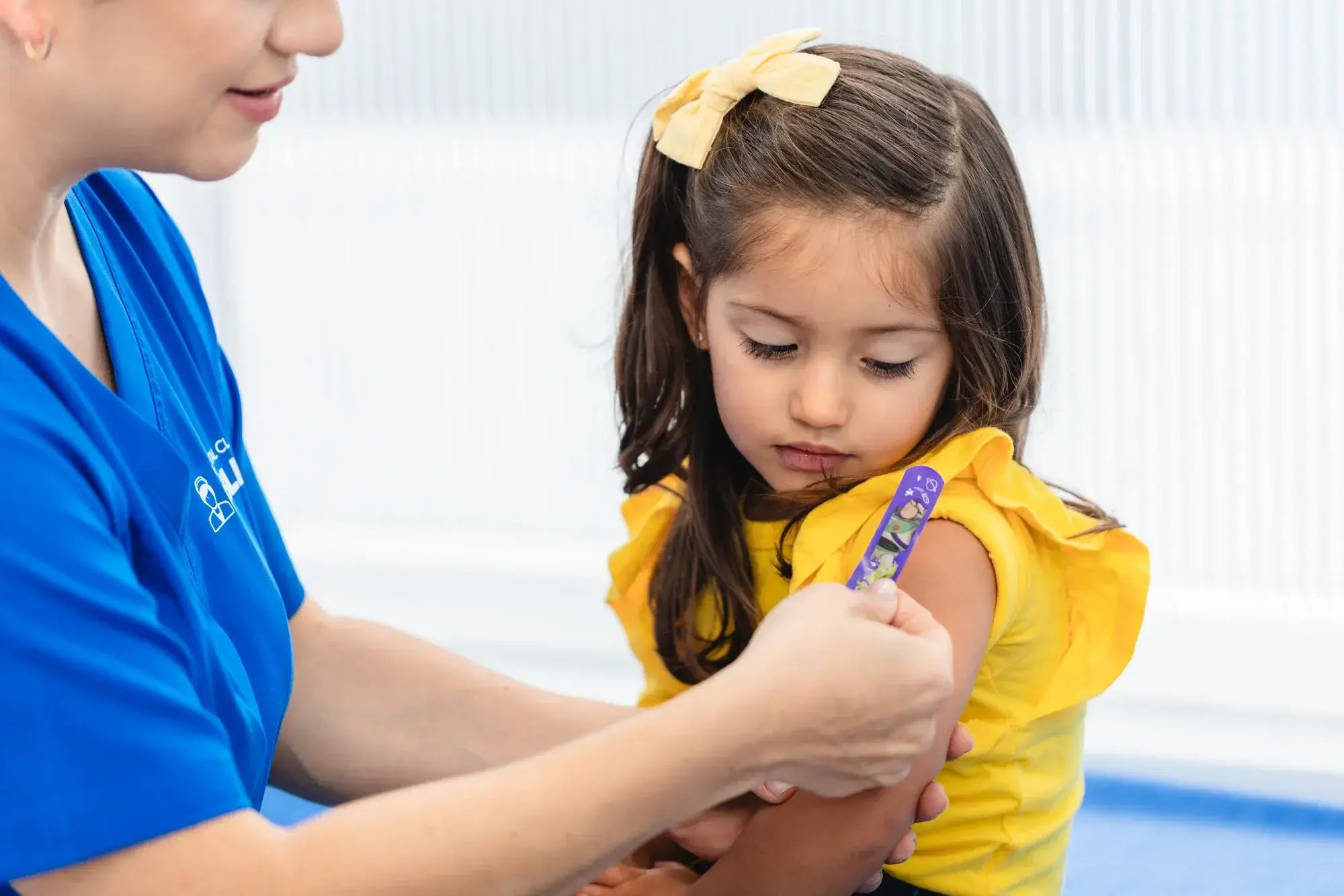 Enfermera aplica curita morada en el brazo de niña tras vacunación pediátrica
