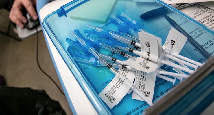 Bandeja médica con jeringas preparadas para vacunación contra COVID-19 con etiquetas de control.