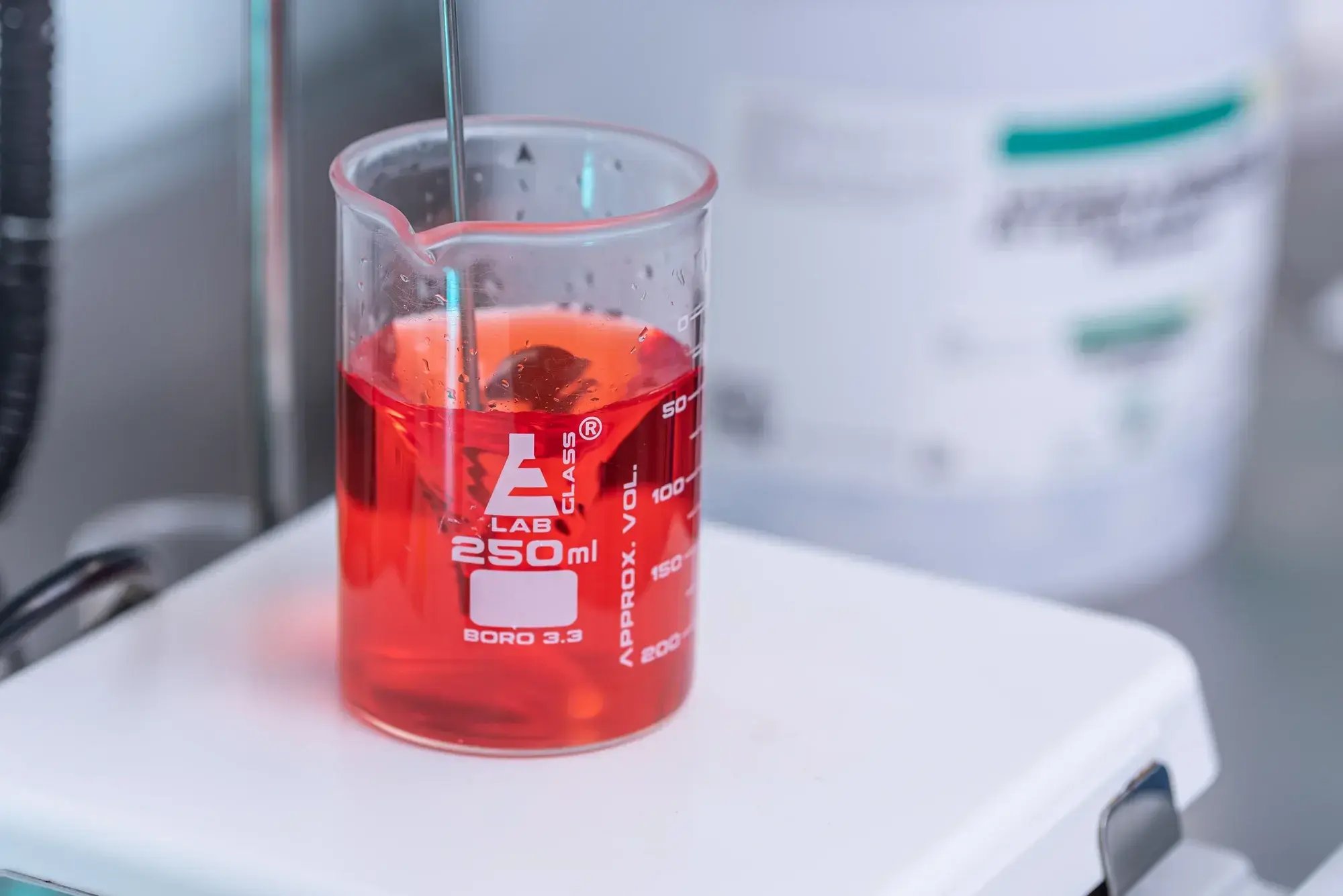 Vaso de precipitados con muestra líquida roja colocado en mesa de laboratorio.