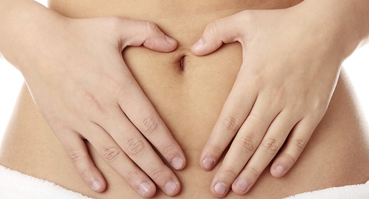 Primer plano del abdomen de una mujer con sus manos colocadas en forma de corazón sobre el ombligo, simbolizando la salud ginecológica.