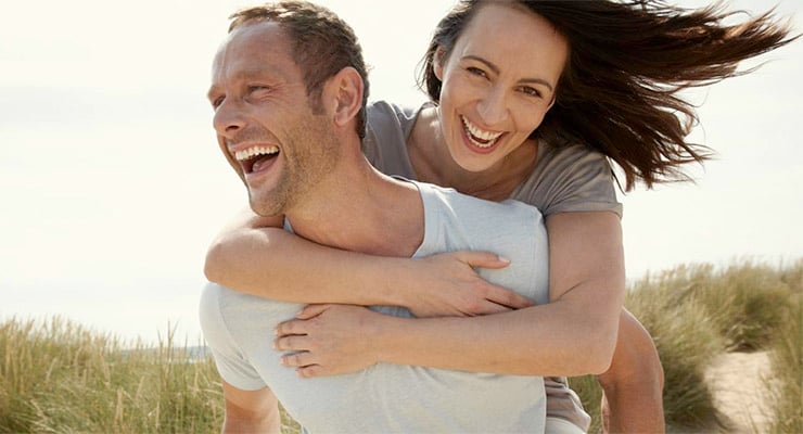 Pareja adulta sonriendo mientras comparten un momento de juego al aire libre en un entorno natural.