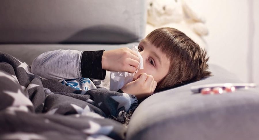 Niño pequeño acostado en cama con una cobija de estrellas, usando un pañuelo para limpiarse la nariz debido a síntomas de virus respiratorio.