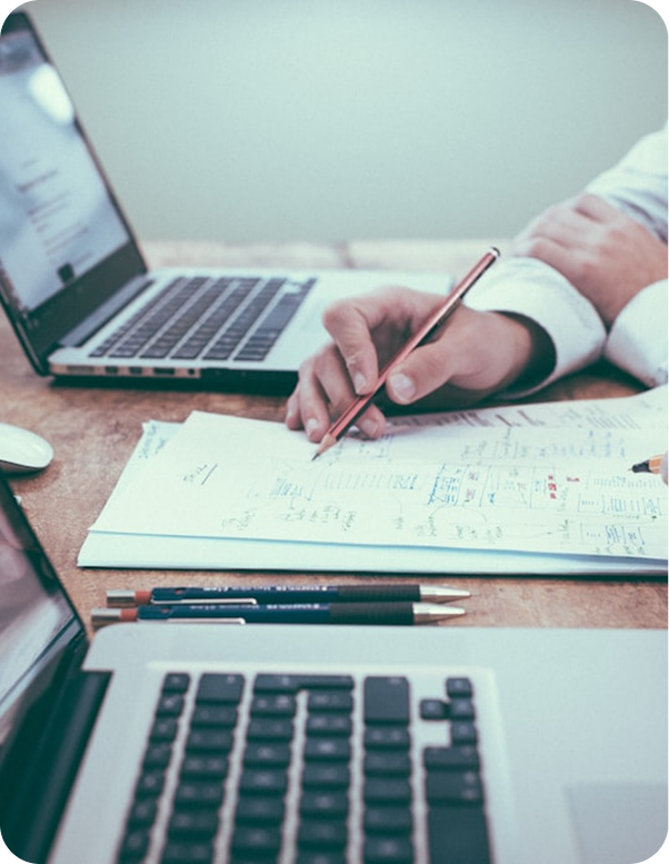Persona escribiendo notas en hoja con laptops abiertas sobre escritorio Persona escribiendo notas en hoja con laptops abiertas sobre escritorio
