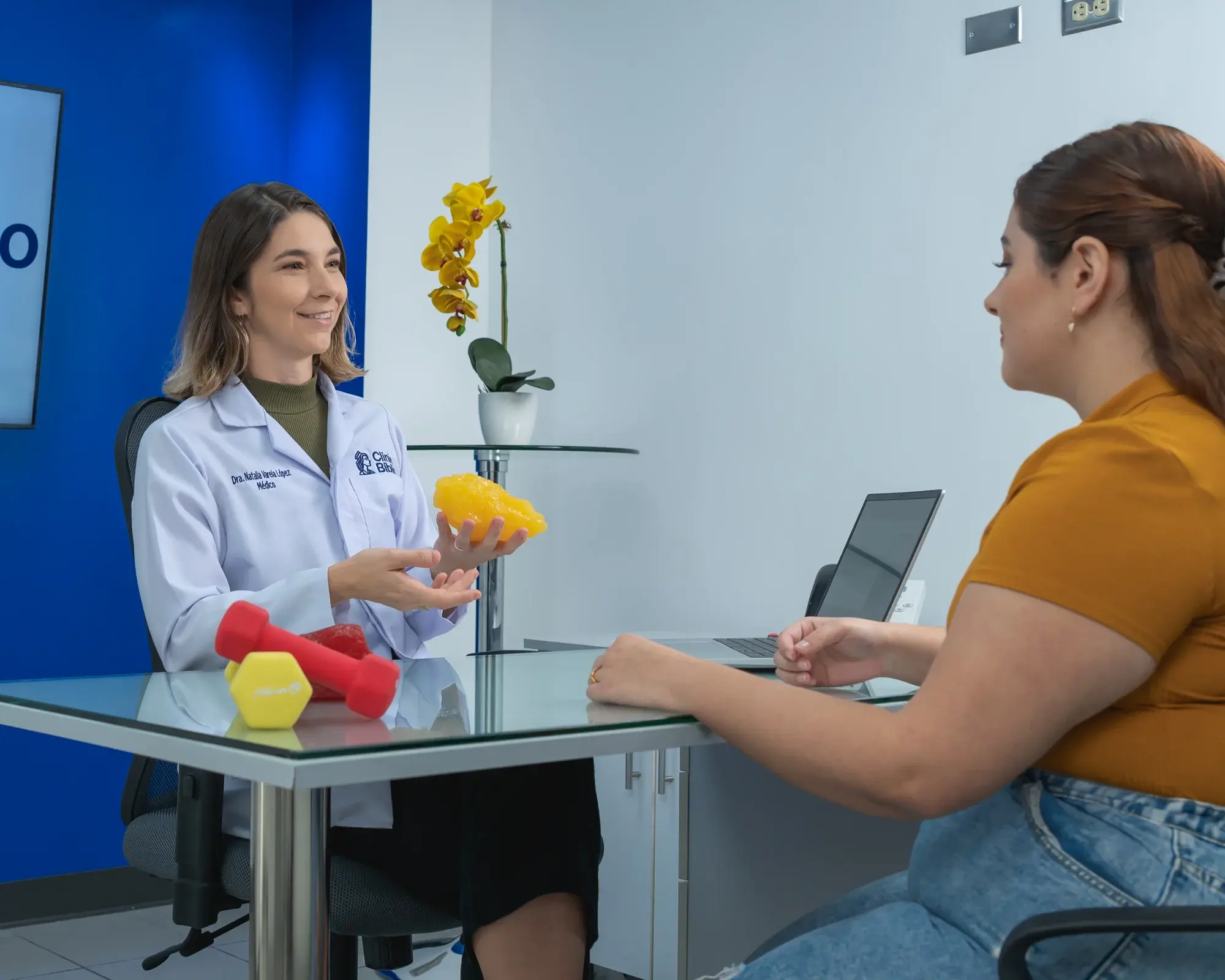 Consulta médica en clínica de metabolismo, doctora mostrando modelo de grasa corporal a paciente.