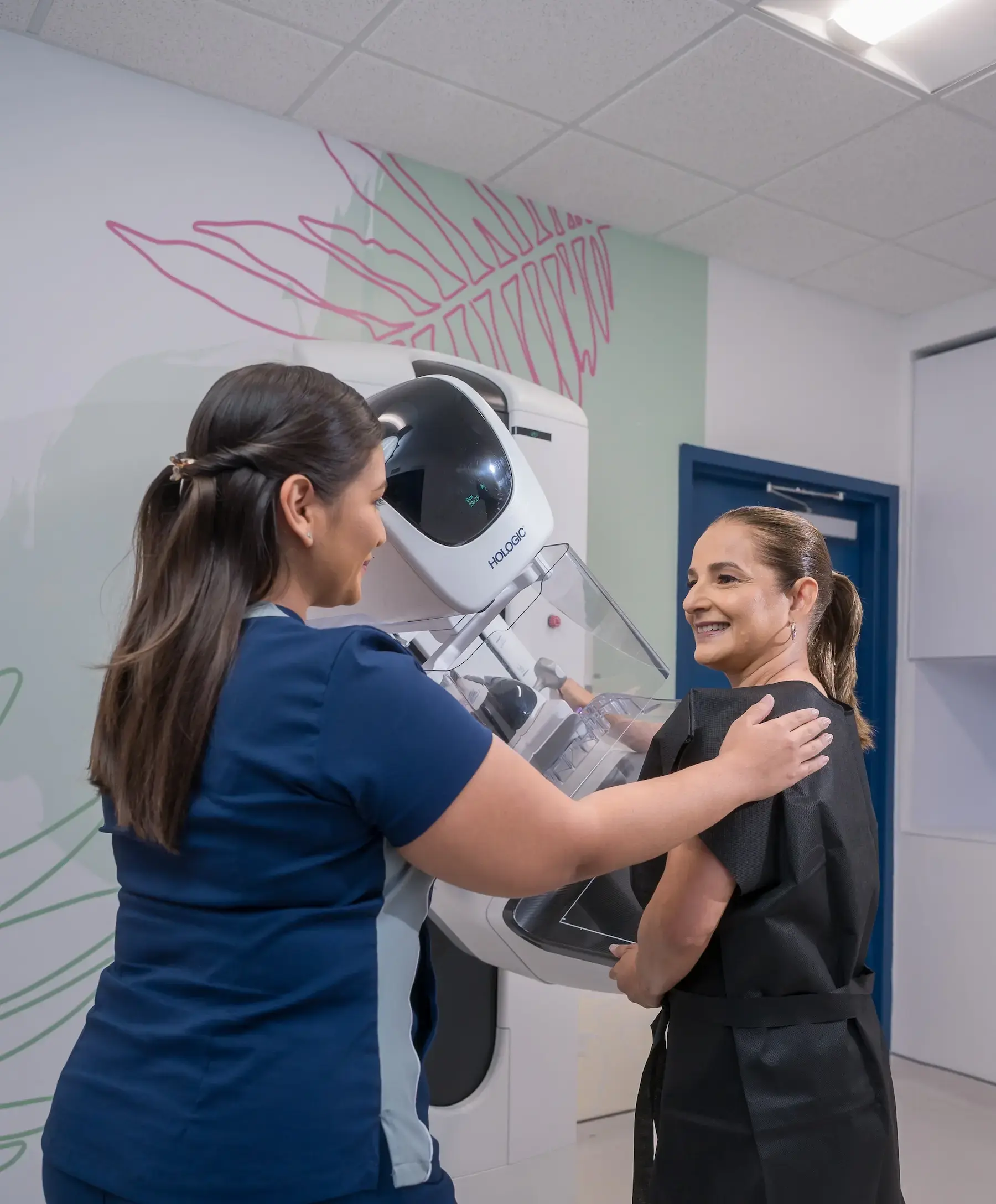 Técnica en radiología del Hospital Clínica Bíblica preparando de manera empática a una paciente frente a un mamógrafo digital Hologic para su examen de seno.