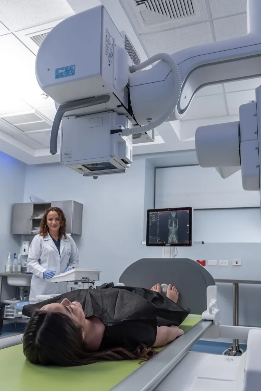 Radiology specialist at Hospital Clinica Biblica operating a Philips robotic digital X-ray and fluoroscopy system for a patient's diagnostic study.