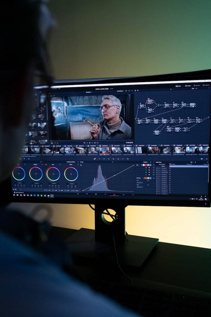 Una persona desde atrás observa un monitor con un software profesional de edición de video y corrección de color.