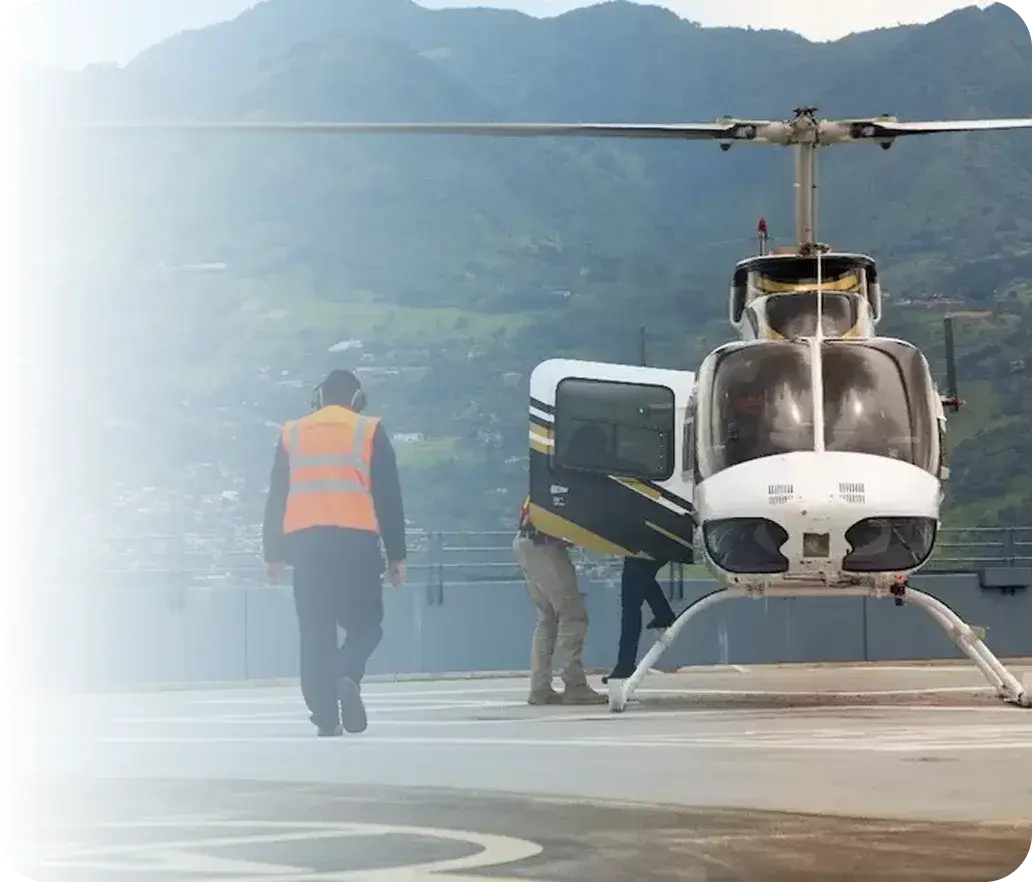 White helicopter on heliport apron as personnel in vests approach.