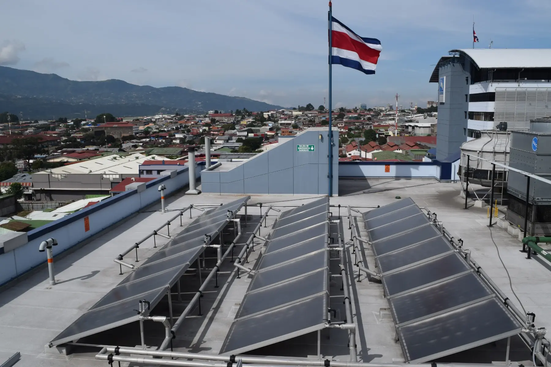 Paneles solares instalados en el techo de un edificio con la bandera de Costa Rica ondeando al fondo.