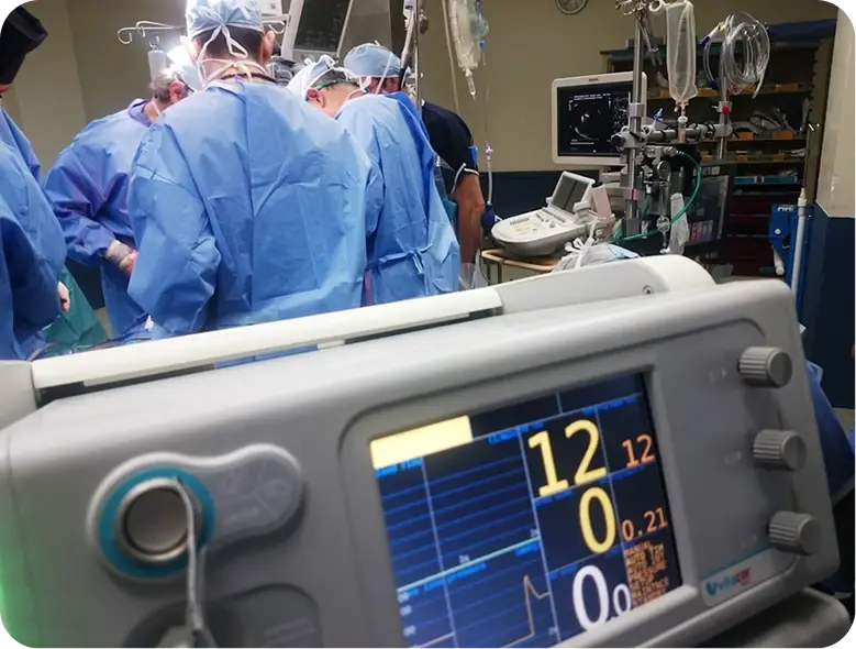 Monitores médicos en primer plano mientras un equipo de cirujanos trabaja en una sala de operaciones.