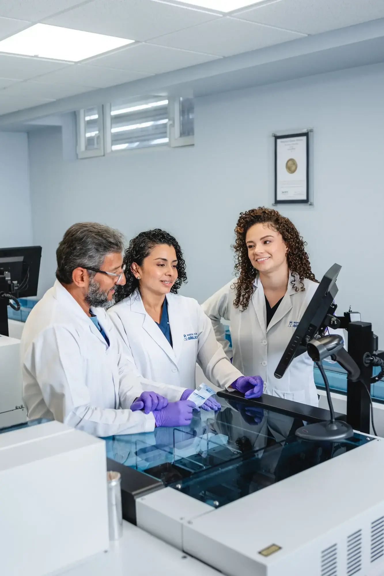 Three doctors in white coats in a lab reviewing samples on a monitor
